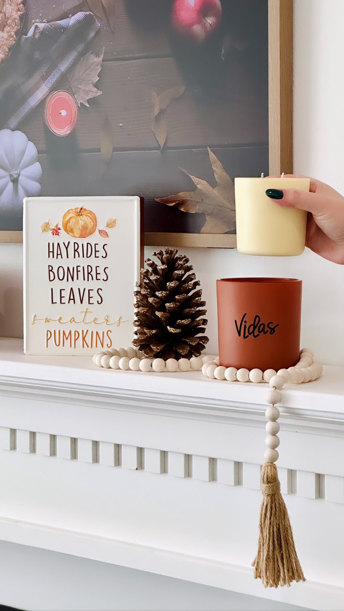 Fall elegance adorns the mantle with a clay candle jar at its center, embraced by seasonal decor. A hand gracefully inserts a candle refill into the jar, combining style and sustainability in a harmonious autumn display.