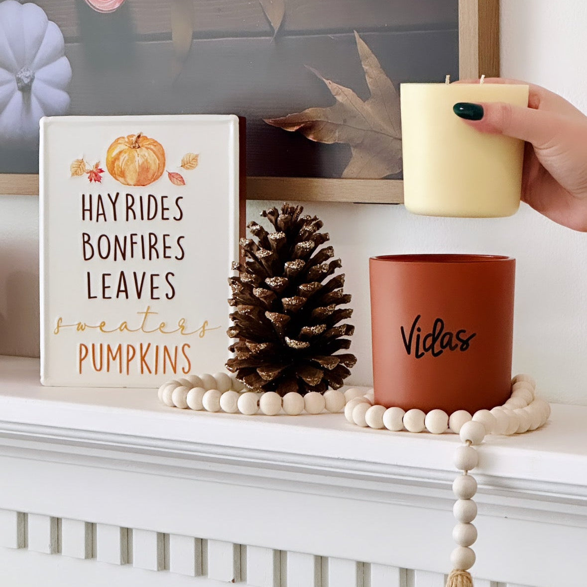 Fall elegance adorns the mantle with a clay candle jar at its center, embraced by seasonal decor. A hand gracefully inserts a candle refill into the jar, combining style and sustainability in a harmonious autumn display.
