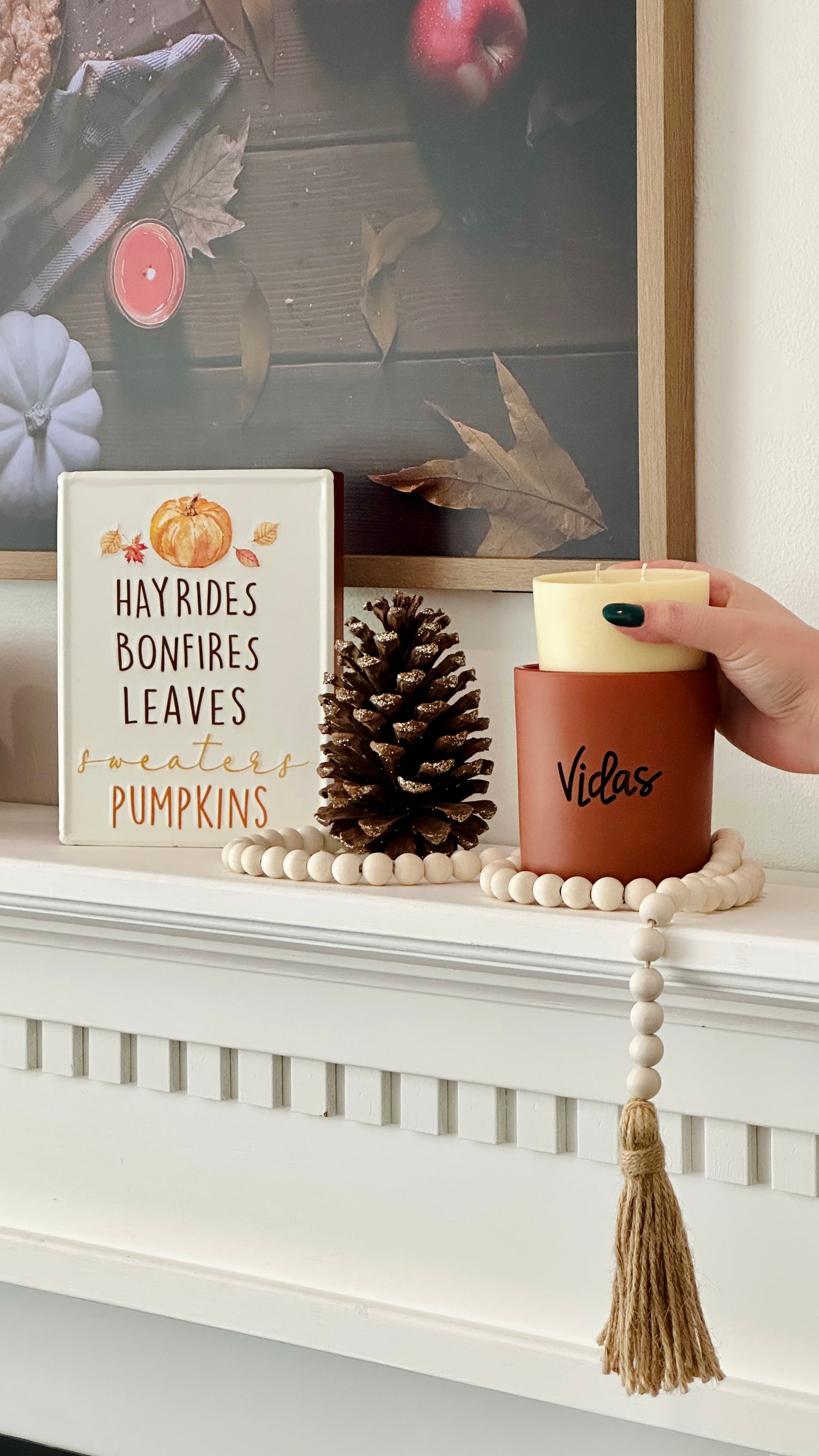 Fall elegance adorns the mantle with a clay candle jar at its center, embraced by seasonal decor. A hand gracefully inserts a candle refill into the jar, combining style and sustainability in a harmonious autumn display.