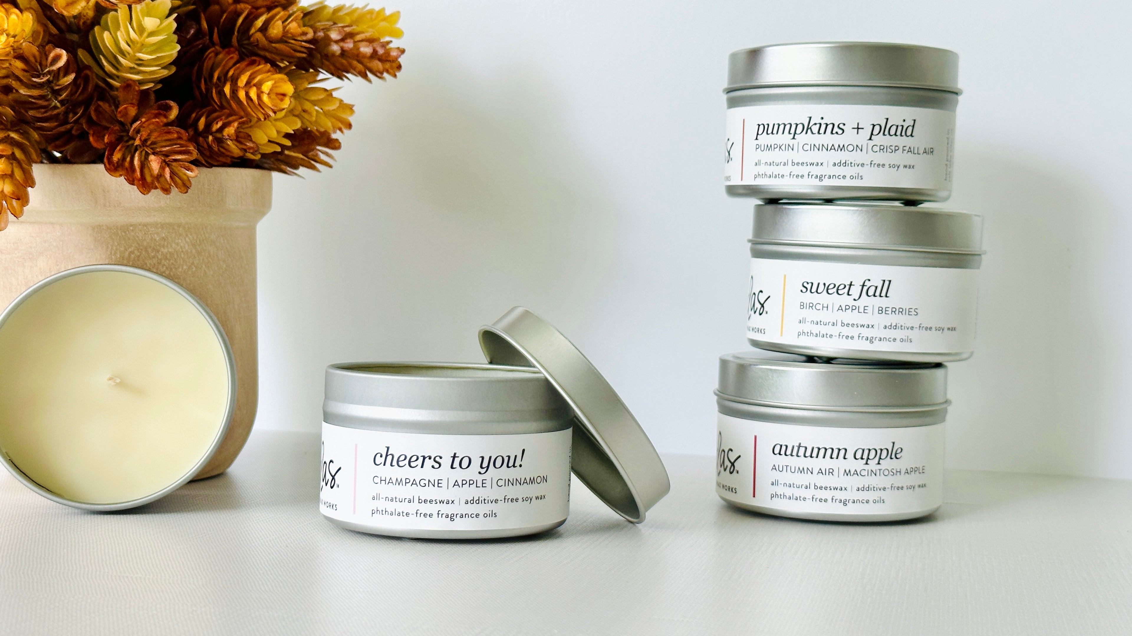Immerse yourself in the essence of autumn. A 3.5oz open candle, shares space with a rustic fall plant on the left. On the right, a delightful stack of three 3.5oz candles stands tall, each ready to kindle the spirit of the season.