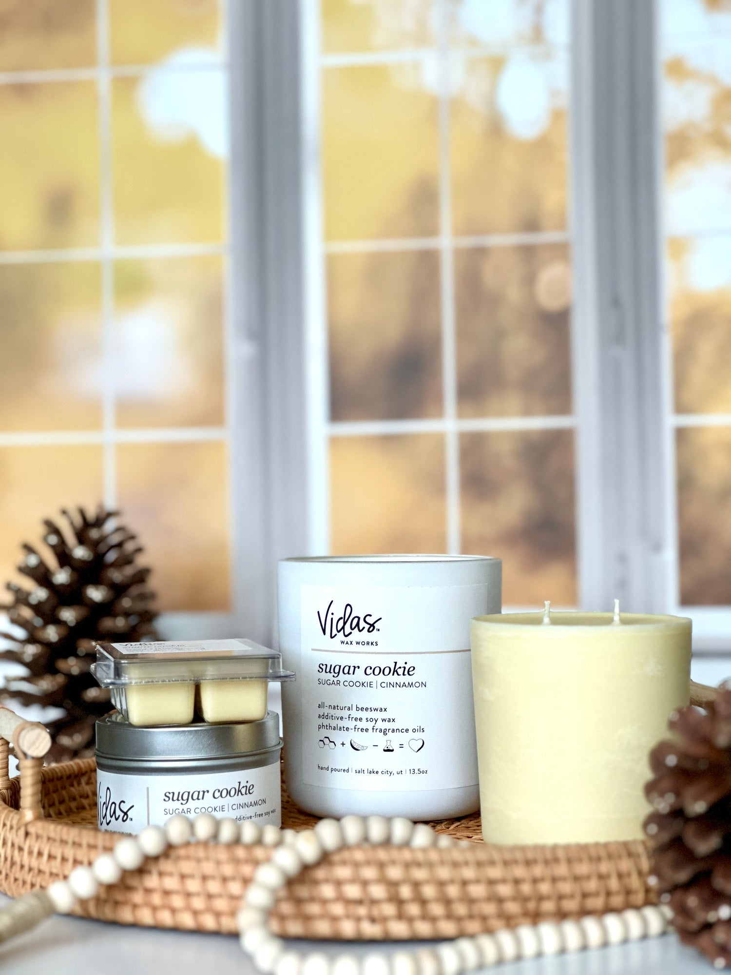 Embrace the autumn ambience with our “Sugar Cookie” scent, a delightful blend of sugar cookie and cinnamon. Against a backdrop of blurred fall-colored leaves outside a window, the collection features a range of offerings: a 13.5oz candle in a chic matte white jar, a 13.5oz candle refill, a compact 3.5oz candle tin, and dainty 2.5oz wax melts. A symphony of scents to elevate your seasonal moments.