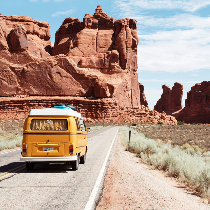 Yellow van on a desert road with red rock formations in the background